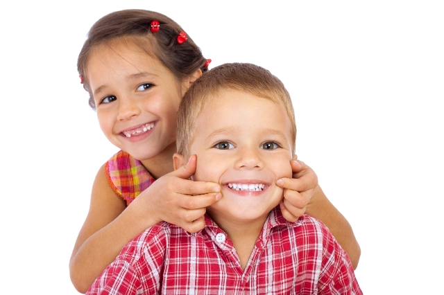 A young girl pulling the sides of a younger boy's mouth open to a smile