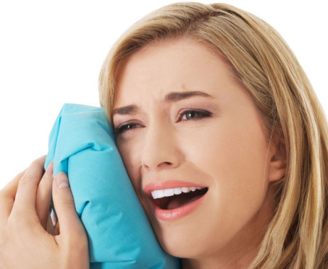 A young blond woman icing the side of her face as she looks in pain