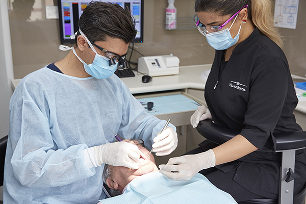 A dentist and assistant performing an operation on a man's mouth