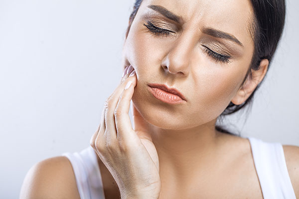 A young brunette woman holding the side of her face in pain