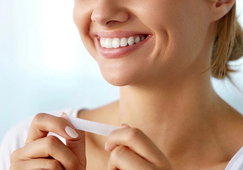 A woman smiling wide while holding a teeth whitening strip