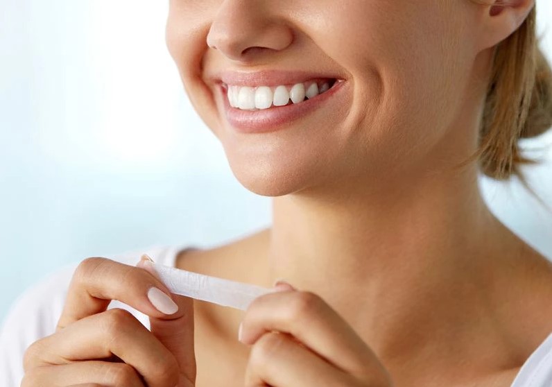 A woman smiling wide while holding a teeth whitening strip