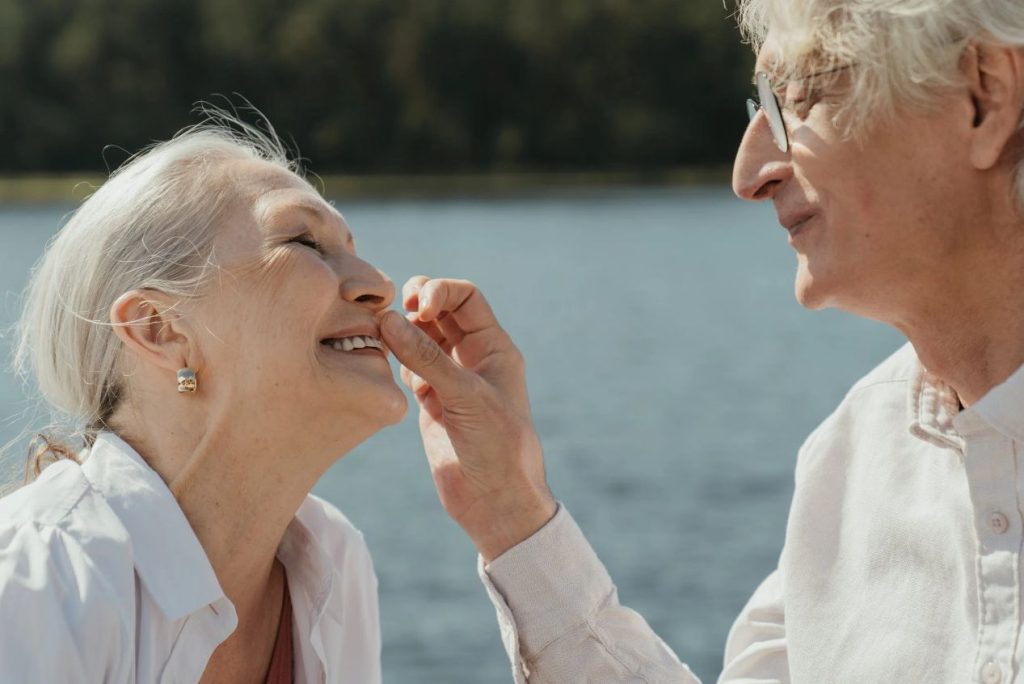 An elderly couple smiling at each other by a lake