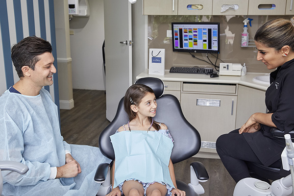 A dentist talking to a young girl in a dental chair